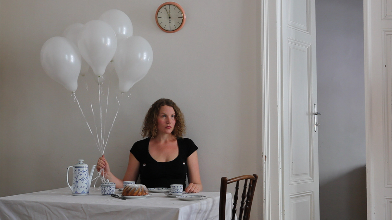Frau mit weissen Luftballonen sitzt am Frühstückstisch